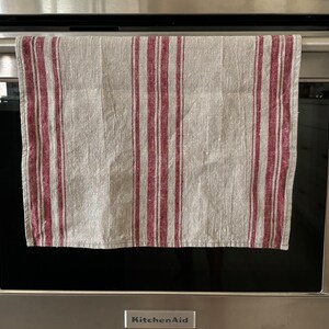 May include: A gray and burgundy striped kitchen towel hanging on a silver oven door handle. The oven door is closed and the brand name "KitchenAid" is visible on the bottom of the door.