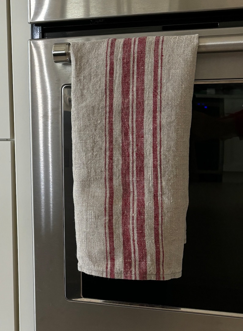 May include: A striped kitchen towel with red and beige stripes hanging on a silver oven door handle.