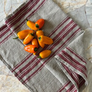 May include: A gray and burgundy striped linen kitchen towel with a pile of yellow and orange bell peppers on top.