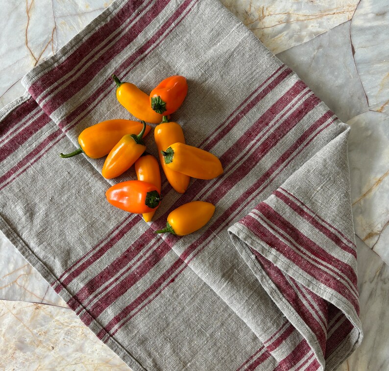May include: A gray and burgundy striped linen kitchen towel with a pile of yellow and orange bell peppers on top.