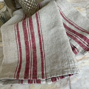 May include: Two linen kitchen towels with red stripes. The towels are folded and stacked on a marble surface.