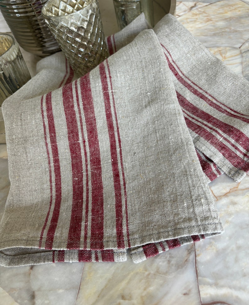 May include: Two linen kitchen towels with red stripes. The towels are folded and stacked on a marble surface.