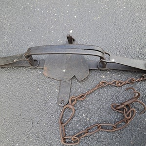 May include: A rusty metal animal trap with a chain and two hooks. The trap is made of metal and has a spring-loaded mechanism.