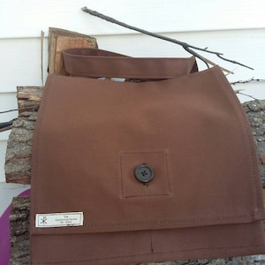May include: A brown canvas messenger bag with a single button closure and a label that reads "The Wandering Parson,  PA, USA".