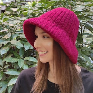 May include: A woman wearing a pink knitted bucket hat. The hat has a wide brim and a ribbed texture.