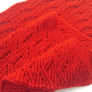 Könnte beinhalten: Ein roter Häkel-Schal mit einem durchbrochenen Muster und Fransen.