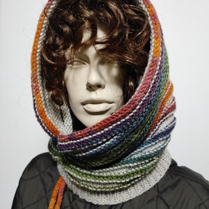 Peut inclure: Un col roulé en tricot rayé coloré avec une capuche. Le col roulé est fait d'un fil doux et texturé et présente une variété de couleurs, notamment l'orange, le rouge, le violet, le bleu, le vert et le gris.