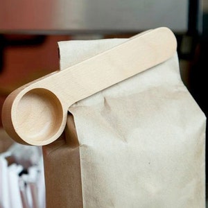 May include: A wooden spoon with a scoop on one end and a handle on the other. The spoon is attached to a brown paper bag.