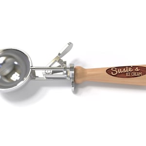 May include: A silver ice cream scoop with a wooden handle. The handle has a brown oval inlay with the text "Susie's Ice Cream" engraved in white.