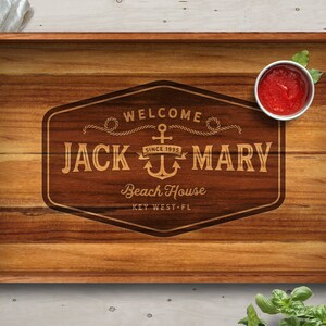 May include: Wooden serving tray with a personalized engraved sign that reads "Welcome Jack & Mary Beach House Since 1995 Key West - FL". The sign features an anchor and rope design.