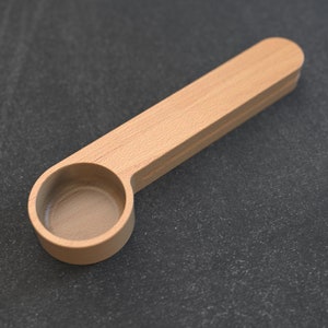 May include: A wooden scoop with a handle. The scoop is made of light brown wood and has a smooth, rounded surface.