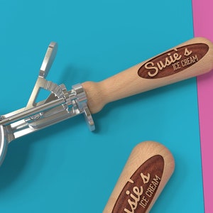 May include: Two silver ice cream scoops with wooden handles. The handles are engraved with the text "Susie's Ice Cream".