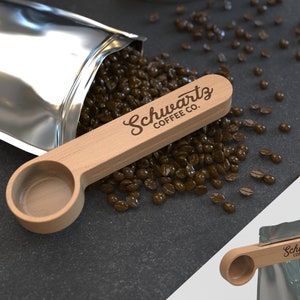 May include: A wooden coffee scoop with the text "Schwartz Coffee Co." engraved on the handle. The scoop is sitting on a pile of coffee beans.
