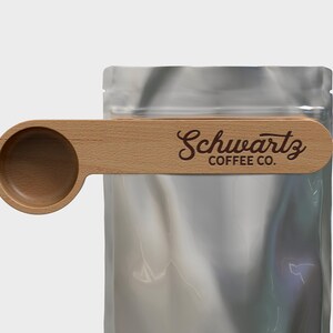 May include: A wooden scoop with a handle that clips onto a bag of coffee. The handle has the text "Schwartz Coffee Co." engraved on it.