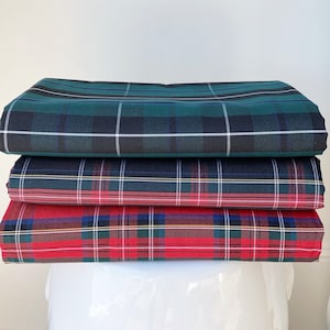 May include: Stack of three plaid fabric swatches in green, blue, and red. The top swatch is a dark green and black plaid, the middle swatch is a blue and green plaid with a thin yellow stripe, and the bottom swatch is a red and green plaid with a thin yellow stripe.