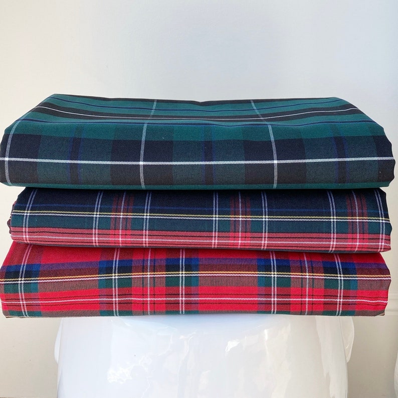 May include: Stack of three plaid fabric swatches in green, blue, and red. The top swatch is a dark green and black plaid, the middle swatch is a blue and green plaid with a thin yellow stripe, and the bottom swatch is a red and green plaid with a thin yellow stripe.
