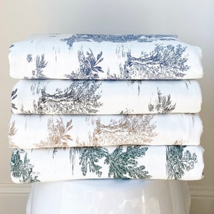 May include: A stack of five white fabric panels with a repeating pattern of black and grey trees and foliage. The fabric is folded and stacked on a white ceramic pedestal.