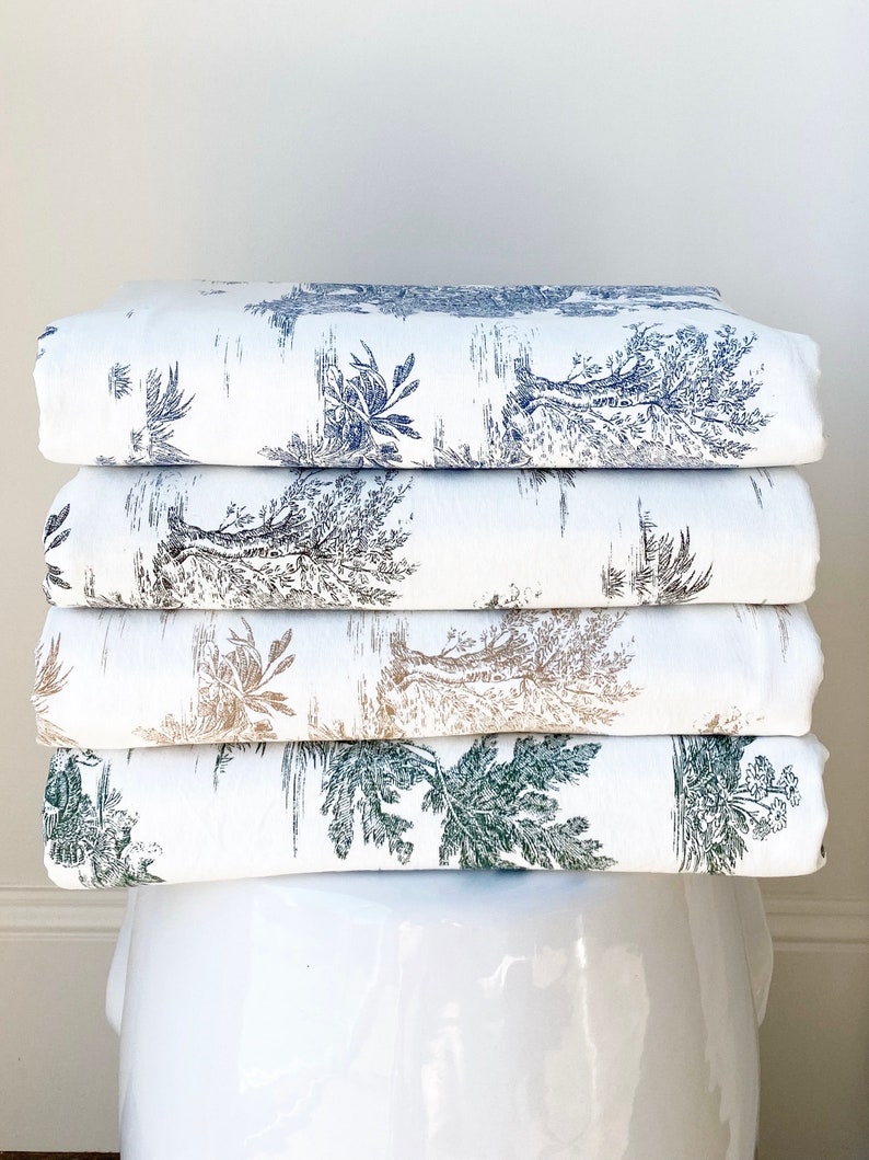May include: A stack of five white fabric panels with a repeating pattern of black and grey trees and foliage. The fabric is folded and stacked on a white ceramic pedestal.