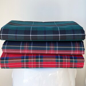 May include: A stack of four plaid fabric squares in green, blue, red, and white. The fabric is folded neatly and the squares are stacked on top of each other.