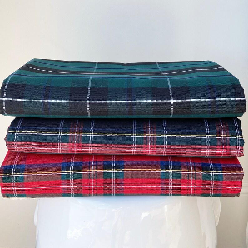 May include: A stack of four plaid fabric squares in green, blue, red, and white. The fabric is folded neatly and the squares are stacked on top of each other.