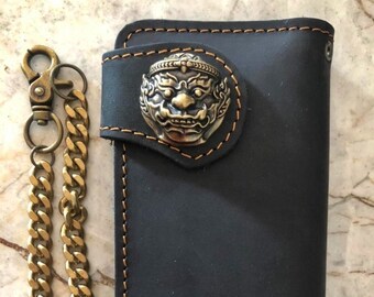 Könnte beinhalten: Schwarze Ledergeldbörse mit einer goldenen Kette und einem dekorativen Metallverschluss mit einer mythischen Kreatur.