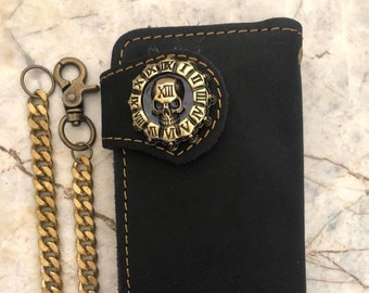 Könnte beinhalten: Eine schwarze Ledergeldbörse mit einer goldenen Kette und einer Totenkopf-Schnalle mit römischen Ziffern drumherum.