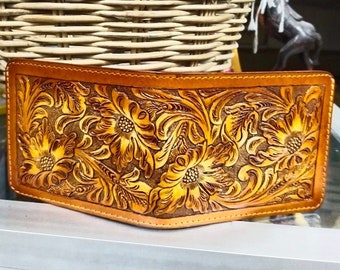 May include: A brown leather wallet with a floral tooled design. The wallet has a stitched edge and a flap closure.