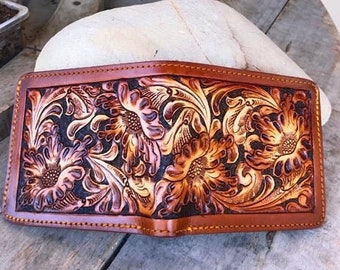 May include: A brown leather wallet with intricate floral tooling. The design features a light brown and dark brown color scheme.