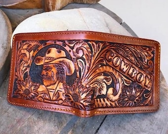 May include: A brown leather wallet with intricate tooled designs, including a cowboy figure wearing a hat and a floral pattern. The word "COWBOY" is embossed on the wallet.