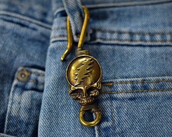 May include: A brass key chain with a skull design and a lightning bolt logo. The key chain is attached to a pair of blue jeans.