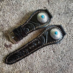 May include: Two black leather watch bands with intricate floral designs and turquoise stone accents.