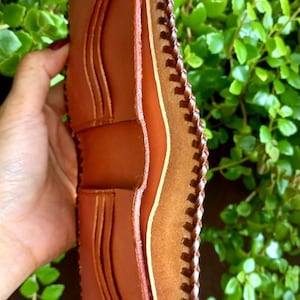 Puede incluir: Una cartera de cuero marr&oacute;n con un borde cosido y m&uacute;ltiples ranuras para tarjetas.