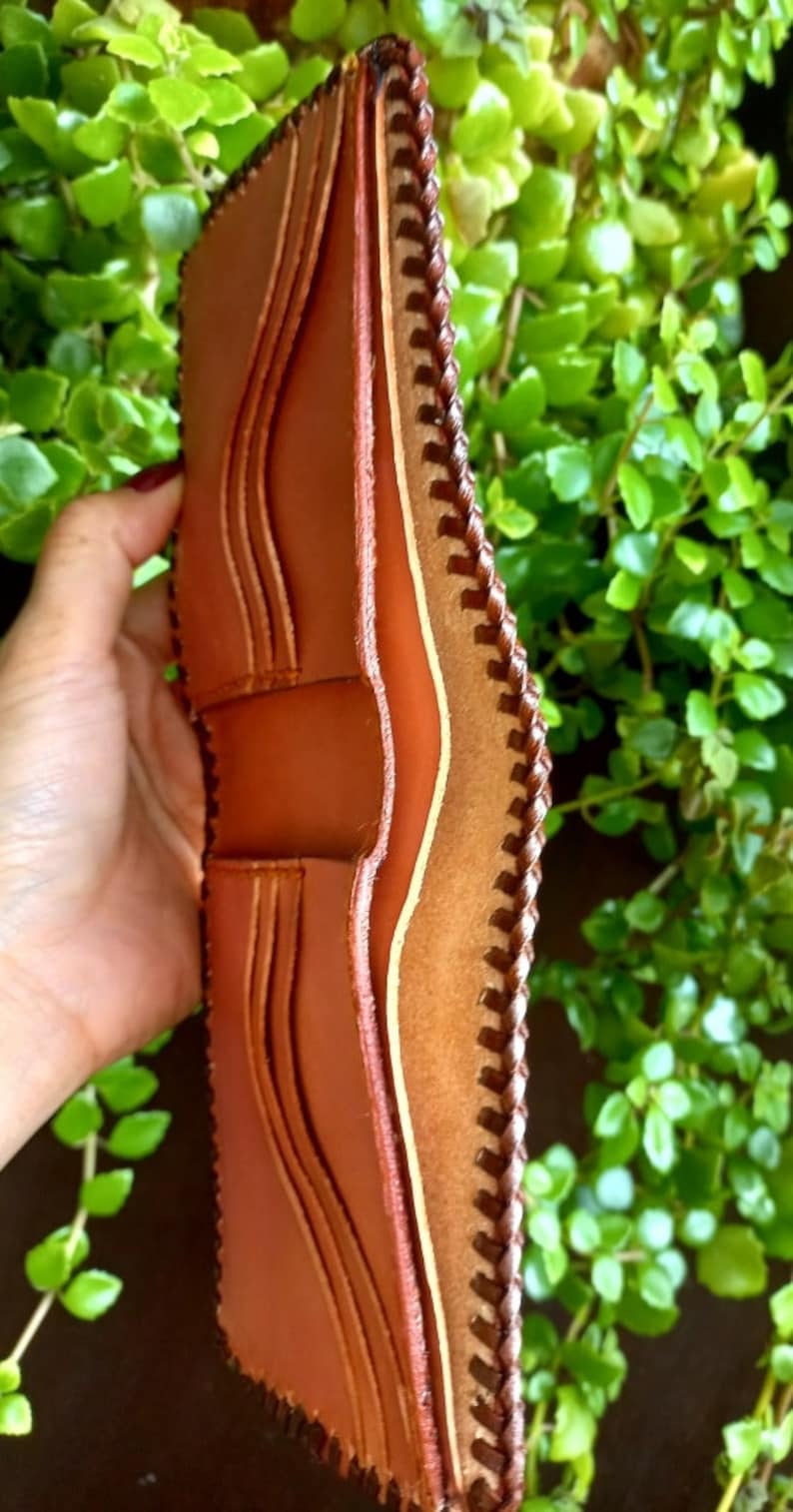 Puede incluir: Una cartera de cuero marr&oacute;n con un borde cosido y m&uacute;ltiples ranuras para tarjetas.