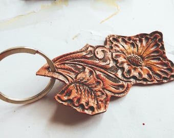 May include: A brown leather keychain with a floral design. The keychain has a silver metal ring.