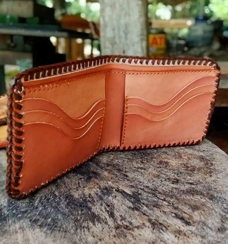 Puede incluir: Una cartera de cuero marr&oacute;n con un borde cosido y m&uacute;ltiples ranuras para tarjetas. La cartera est&aacute; abierta y el interior es visible.