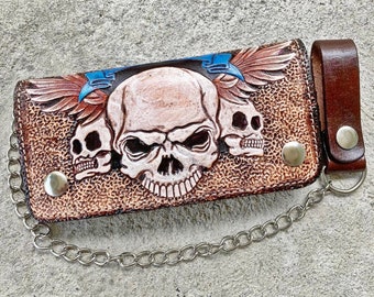 Könnte beinhalten: Eine braune Ledergeldbörse mit Totenkopf-Design und einer Kette. Die Geldbörse hat eine Klappe mit einem Totenkopf- und Flügel-Design. Die Geldbörse ist aus echtem Leder und hat eine Kette.