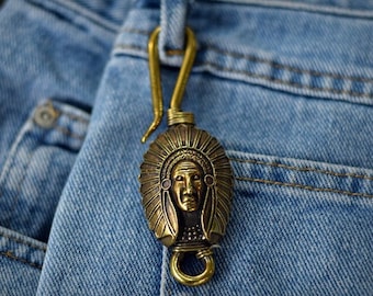 May include: A brass key chain with a detailed Native American chief head design. The keychain is attached to a pair of blue jeans.
