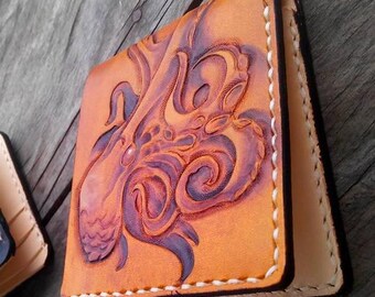 May include: A brown leather wallet with a tooled design of an octopus. The wallet has white stitching around the edges.