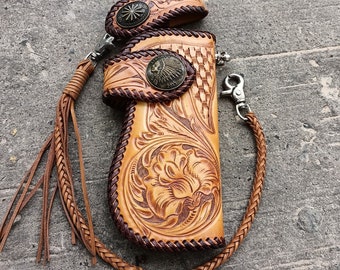 May include: A brown leather wallet with intricate floral carvings and a braided leather chain. The wallet has a snap closure and a metal button with an Indian head design.