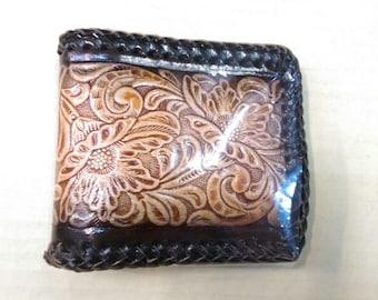 May include: A brown leather wallet with a floral embossed design. The wallet has a black braided trim around the edges.