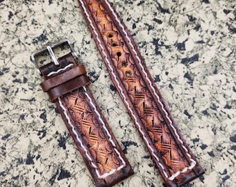 Könnte beinhalten: Zwei braune Lederarmbänder mit weißen Nähten und einem geprägten Muster. Die Armbänder liegen auf einer strukturierten Oberfläche.