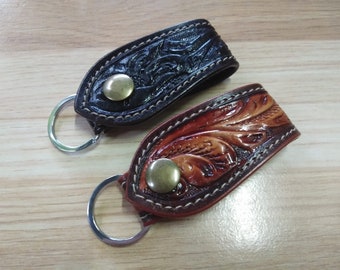 May include: Two leather keychains with a decorative floral design. One keychain is brown and the other is black. Both keychains have a metal ring and a brass button.
