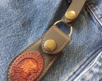 May include: A brown leather key chain with a metal ring and a snap closure. The key chain has a brown leather eagle emblem embossed on it.