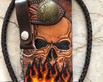 Könnte beinhalten: Braune Ledergeldbörse mit Totenkopf-Design und Flammendetails. Verfügt über eine Liberty-Münze aus Metall und einen geflochtenen Lederriemen mit Kette und Verschluss. Die Geldbörse ist etwa 18 cm hoch.