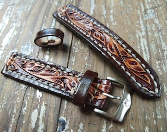 Könnte beinhalten: Ein braunes Lederarmband mit weißen Nähten und einem Blumenmuster. Das Armband hat eine silberne Schnalle.