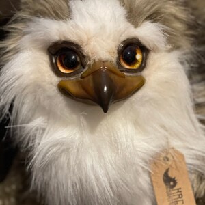 Puede incluir: Primer plano de un juguete de peluche con la cara blanca, ojos marrones y un pico marr&oacute;n. El juguete tiene un patr&oacute;n de pelaje blanco y marr&oacute;n. El juguete tiene una etiqueta que dice "KreaLo Design & Toys".