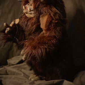 K&ouml;nnte beinhalten: Eine braune, pelzige Monsterfigur mit detailliertem Gesicht, H&ouml;rnern und roten Augen. Die Kreatur hat einen bedrohlichen Ausdruck und steht aufrecht. Die Figur besteht aus einem weichen, pl&uuml;schigen Material.