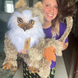 Puede incluir: Una persona sosteniendo un gran juguete de peluche marr&oacute;n y blanco con una cola larga. El juguete tiene una cara de p&aacute;jaro con ojos grandes de color naranja y un pico. El juguete tiene una etiqueta que dice "Harecalo Creations".