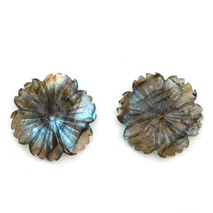May include: Two carved labradorite flower cabochons with iridescent blue and green hues. The cabochons are a light brown color and have a detailed carved flower design.