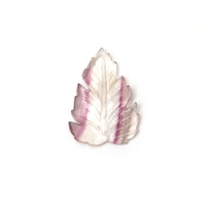 May include: A carved leaf pendant made of clear and purple fluorite. The leaf is detailed with veins and has a natural, organic shape.